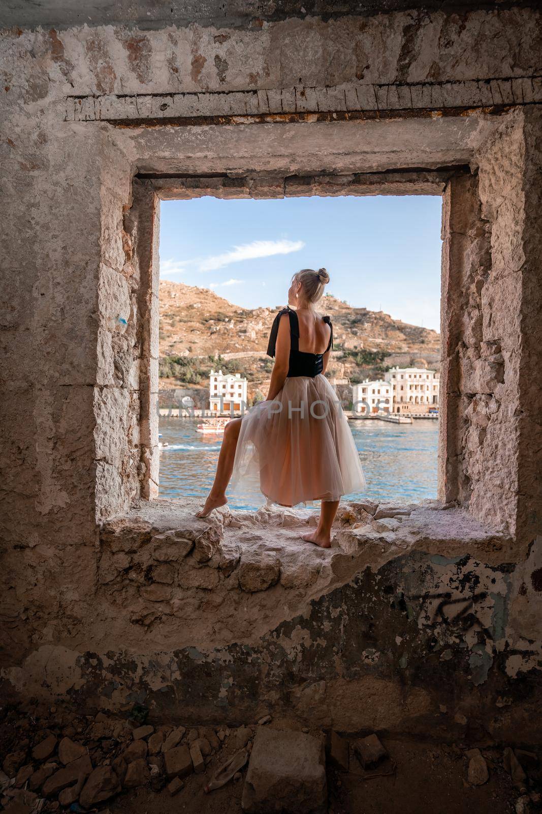 Side view portrait of a relaxed woman breathing fresh air at the seaside. She stands on the window in the old building. by Matiunina