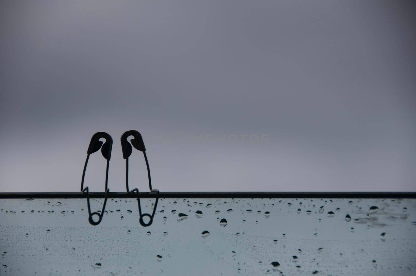 Safety pin couple sitting on glass wall with customizable space for text and ideas. Love and romance concept.
