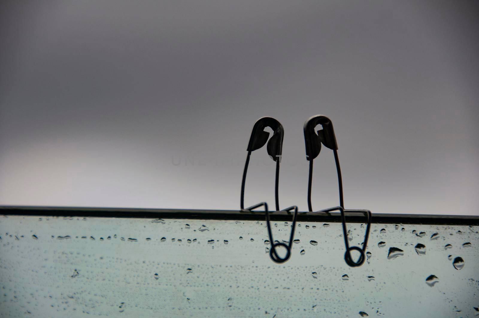 Safety pin couple sitting on glass wall with customizable space for text and ideas. Love and romance concept.