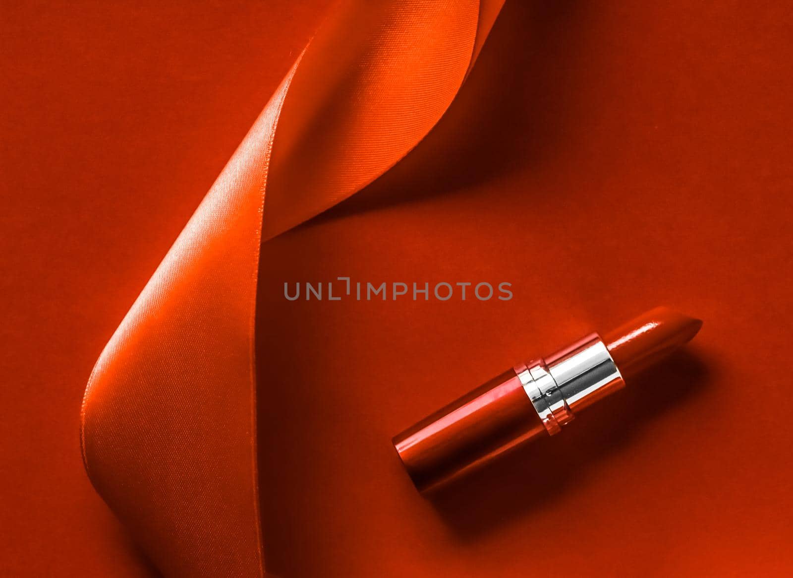 Cosmetic branding, glamour lip gloss and shopping sale concept - Luxury lipstick and silk ribbon on orange holiday background, make-up and cosmetics flatlay for beauty brand product design