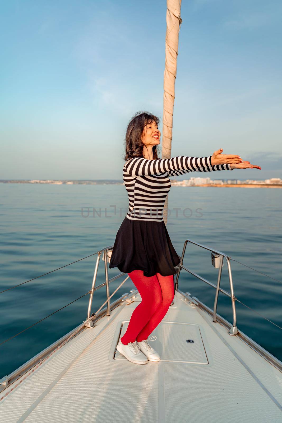 Woman standing on the nose of the yacht at a sunny summer day, breeze developing hair, beautiful sea on background by Matiunina