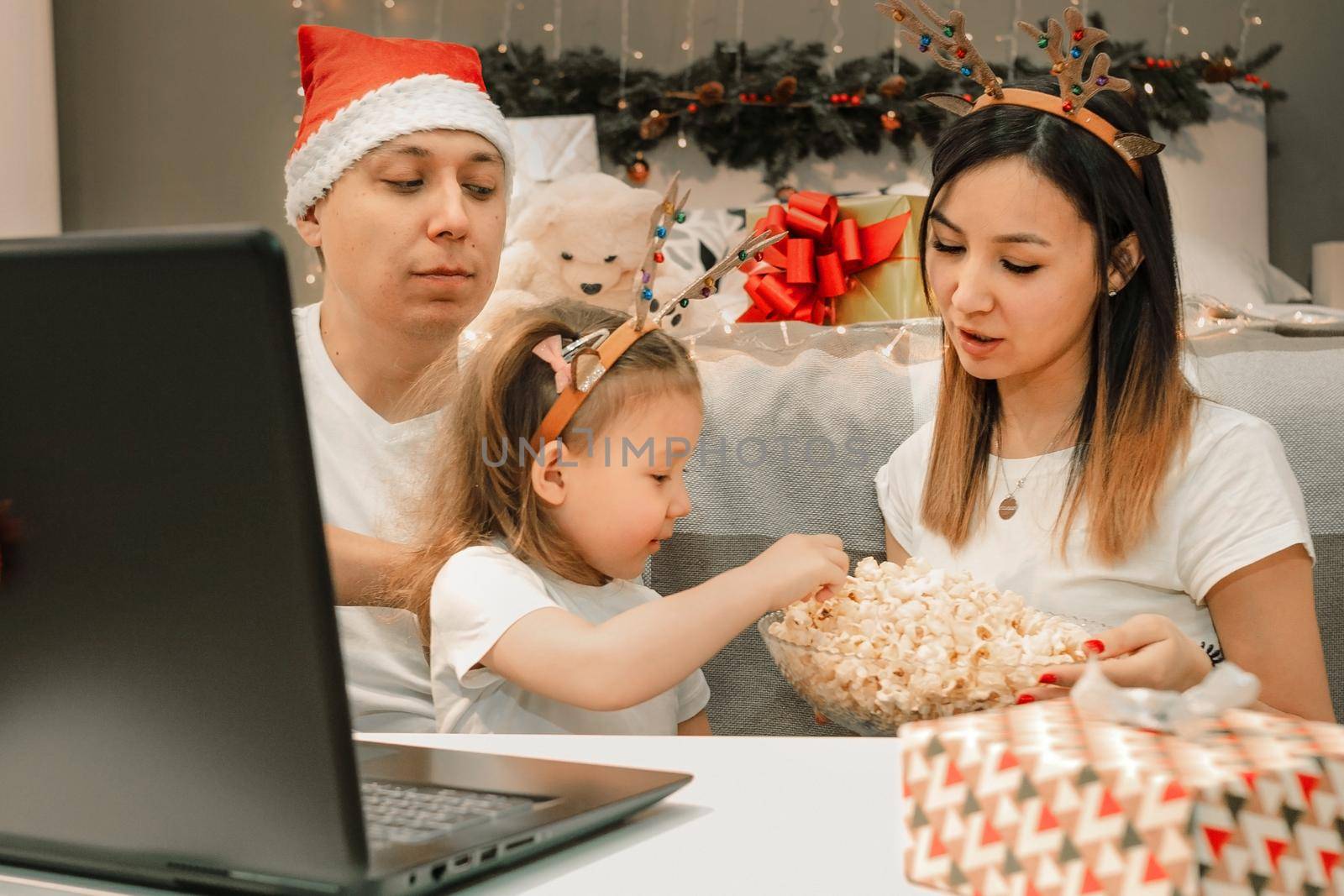 Cozy family christmas with father mother and child girl daughter, watching video on laptop in bedroom, happy fun and xmas holiday together at movie night or via video link, authentic festive lifestyle