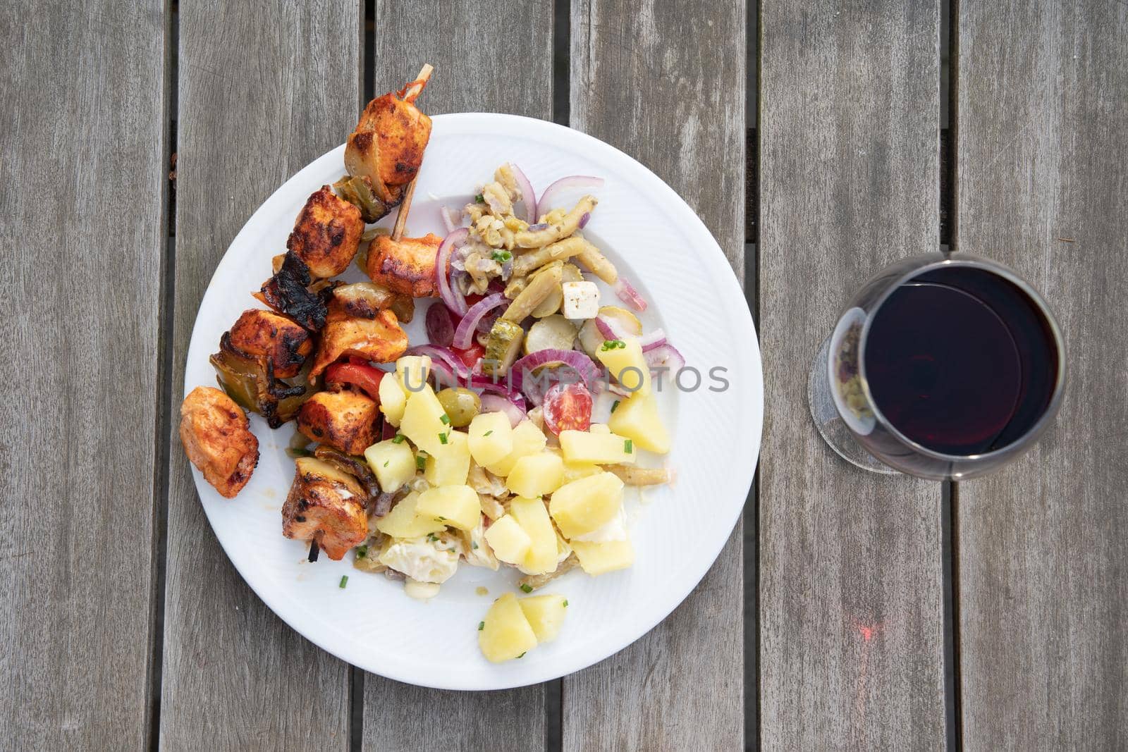 summer picnic food, homemade chicken barbecue with vegetable salad and cold boiled potatoes, red wine in a glass, traditional belgian dish serving. High quality photo