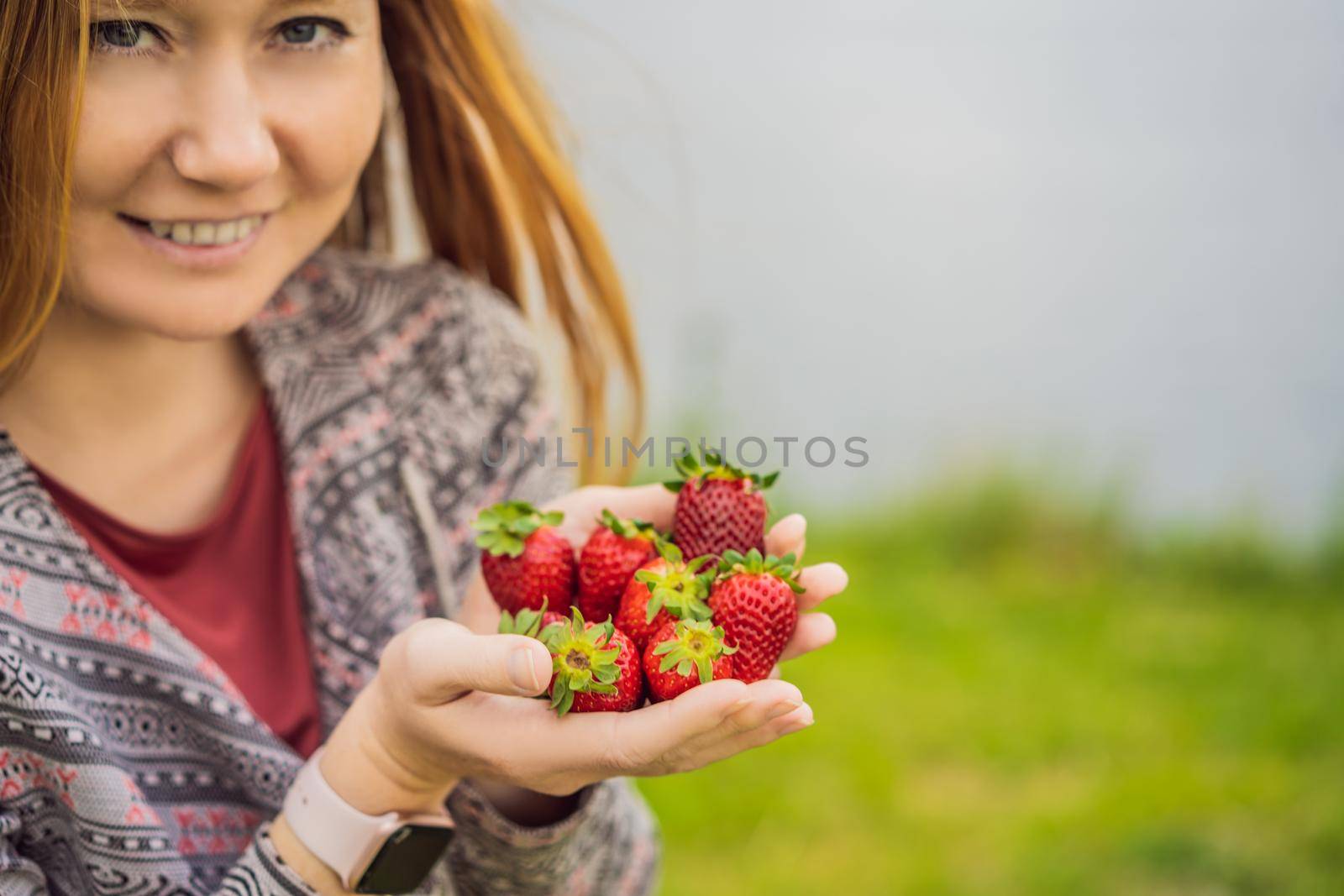 Young attractive woman eating a strawberry, outdoors.