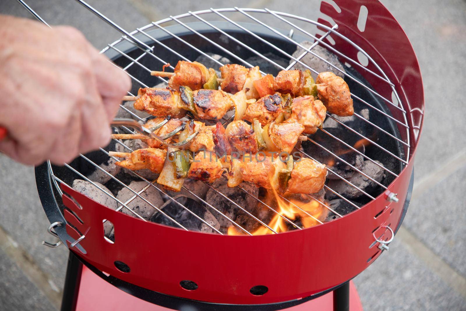man flipping chicken skewers on barbecue grill over hot coals, summer delicacies, vacation food on terrace. High quality photo