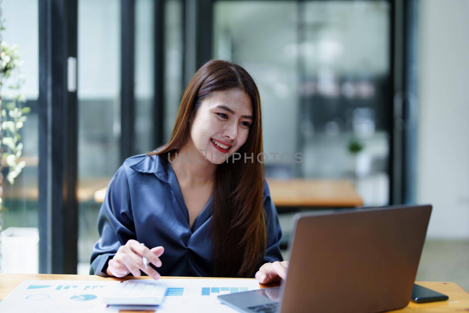 Portrait of an Asian female employee using computer with a smiling face as she works the next morning.
