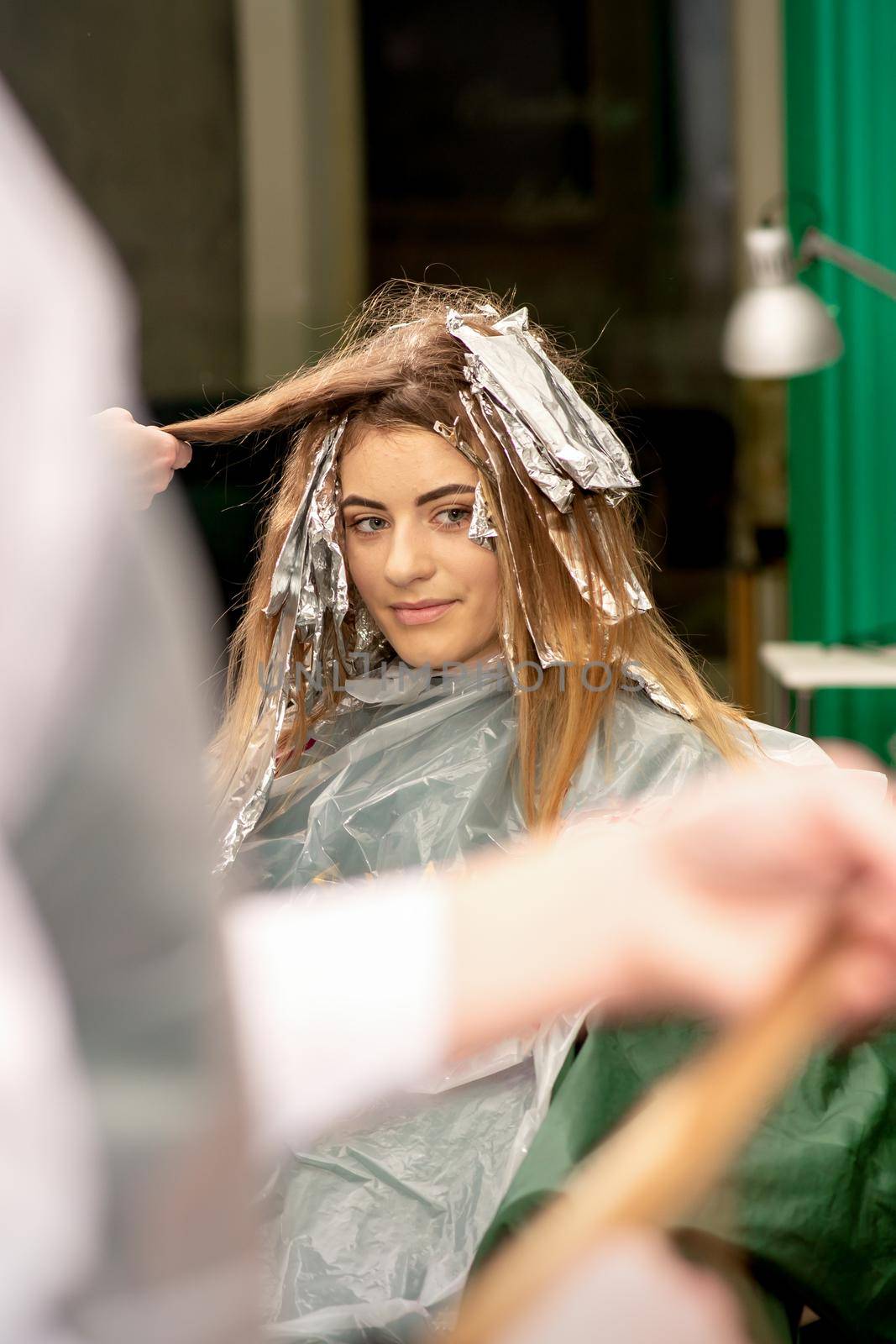 Portrait of a beautiful young caucasian woman who is smiling getting dyeing her hair with foil in a beauty salon. by okskukuruza