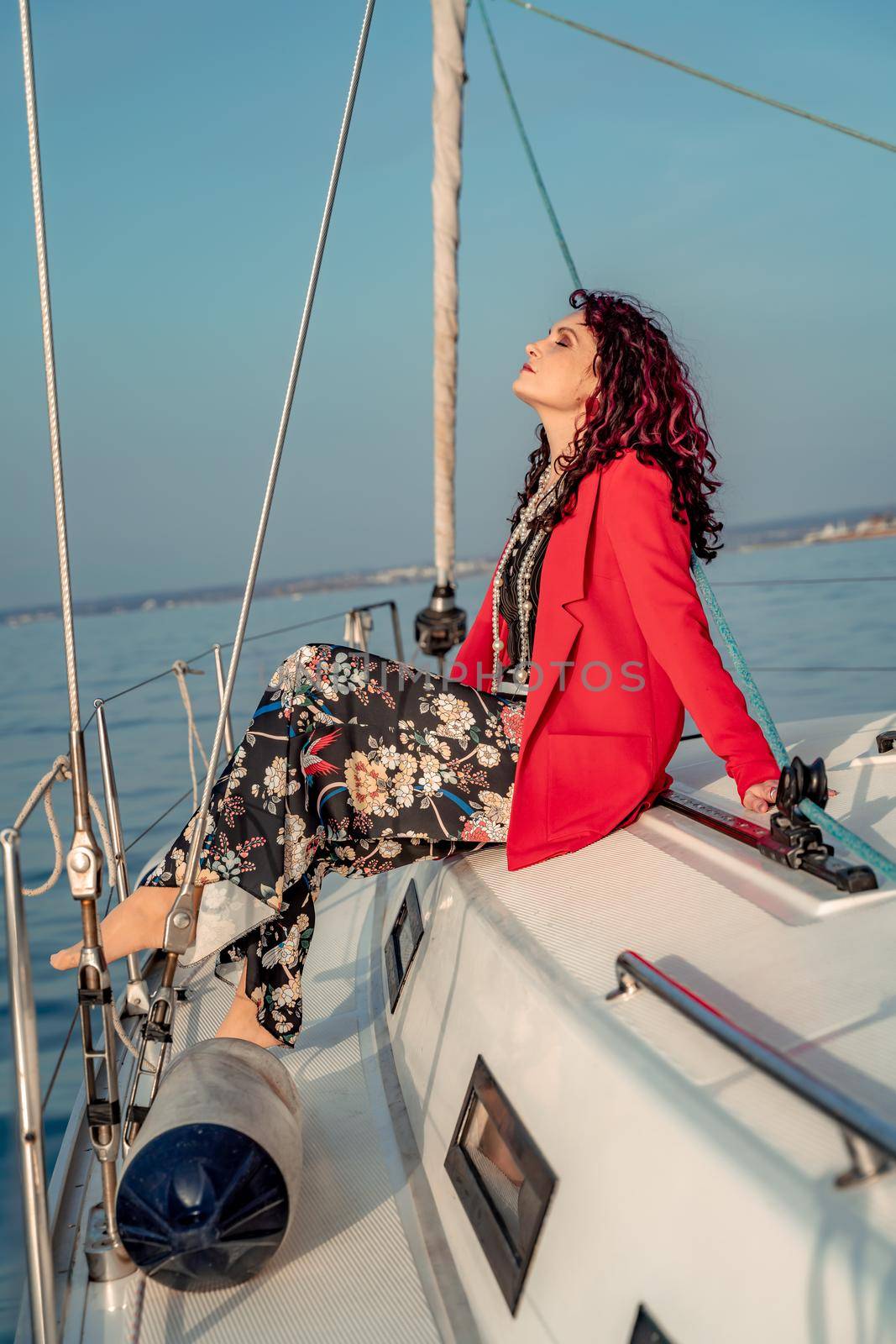 A woman sits on the bow of a yacht on a sunny summer day, the breeze develops her hair, a beautiful sea is in the background by Matiunina