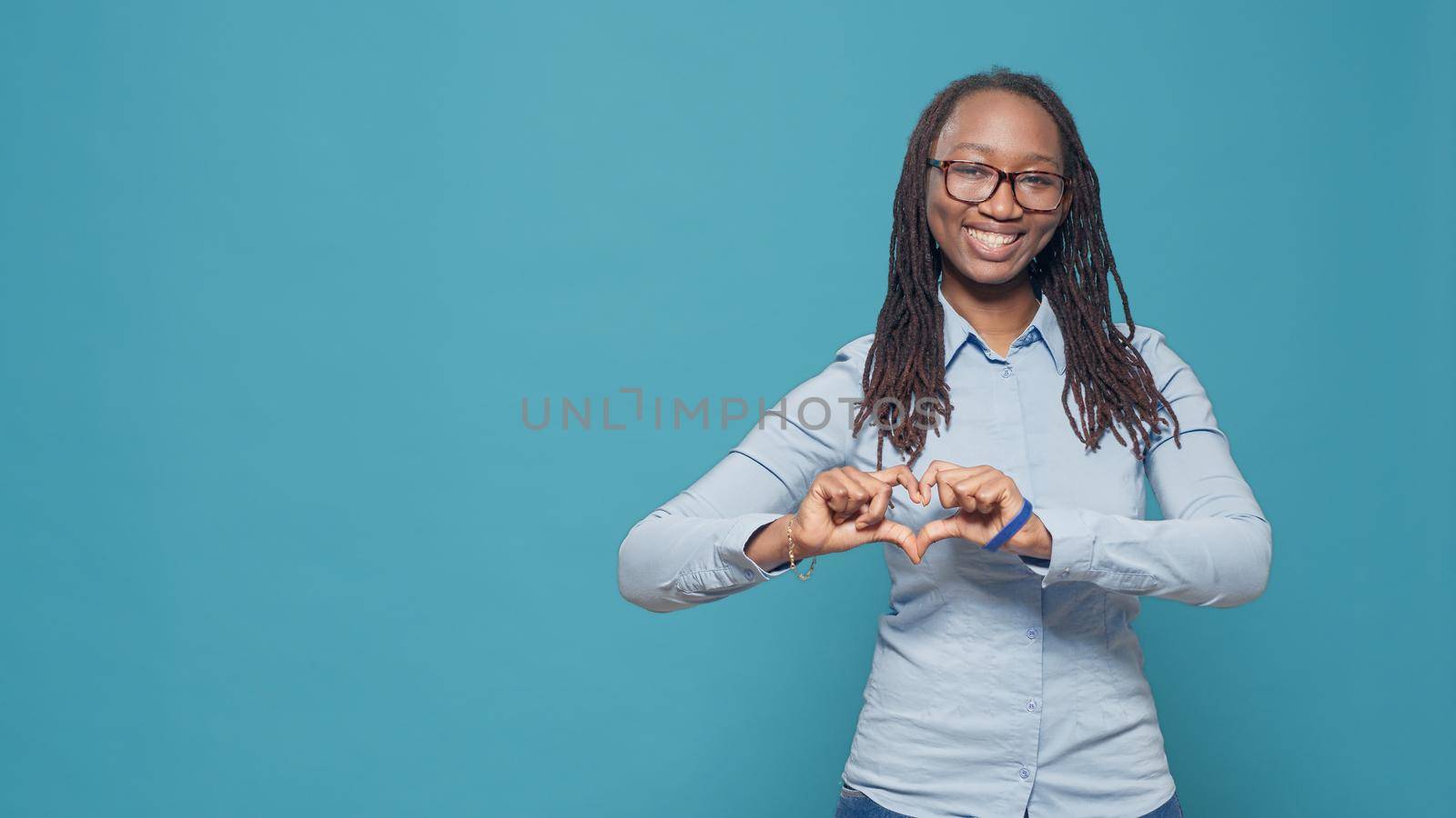 Woman doing heart shape with hands on camera, showing romantic gesture and happy valentines day symbol. Expressing love feelings and gratitude on studio background, romance sign.