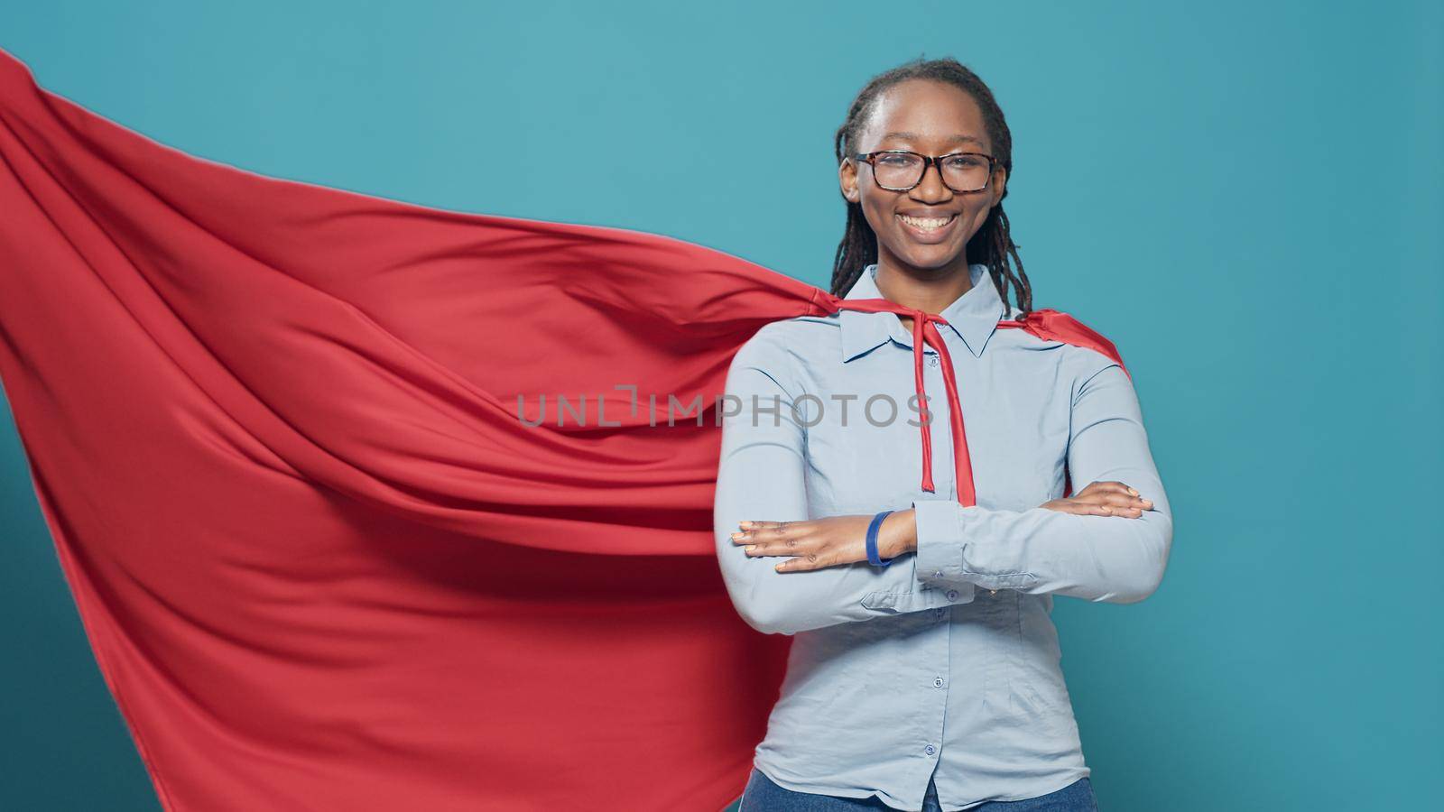 African american woman posing as superhero with red flying cape, wearing cartoon comic costume with cloak on camera. Feeling confident and powerful as hero, strong action character.