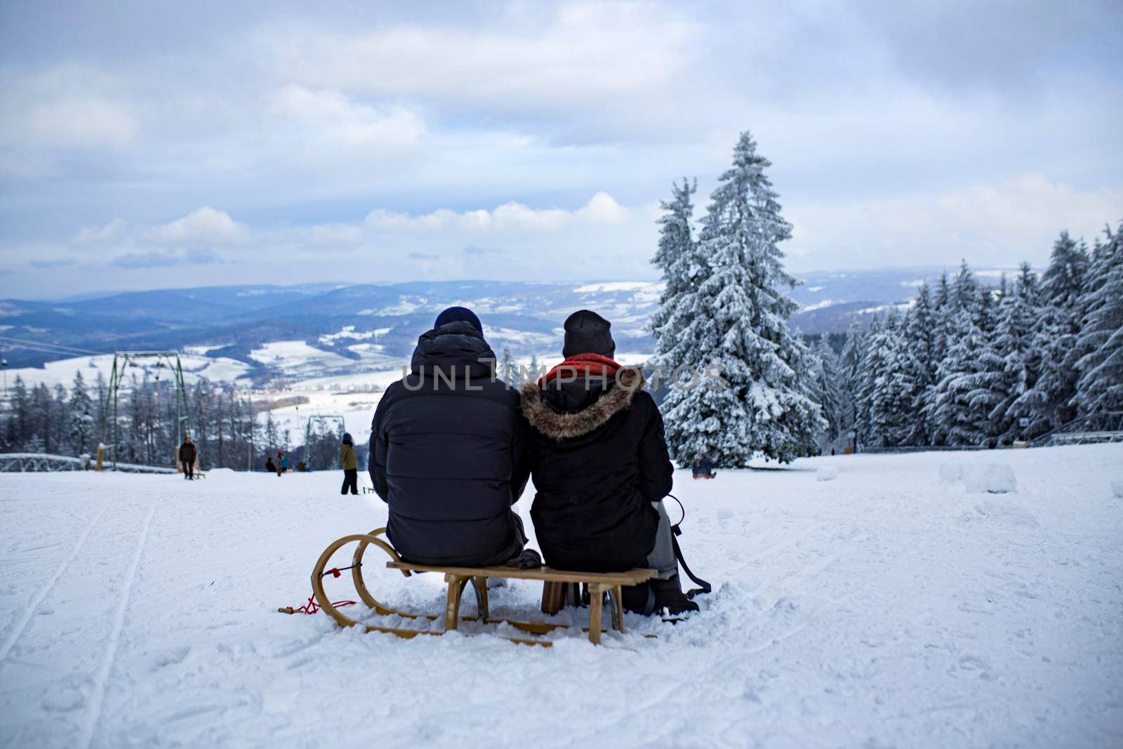 the backs of people sitting on a sled against the background of a snow-covered ski slope in winter by Costin