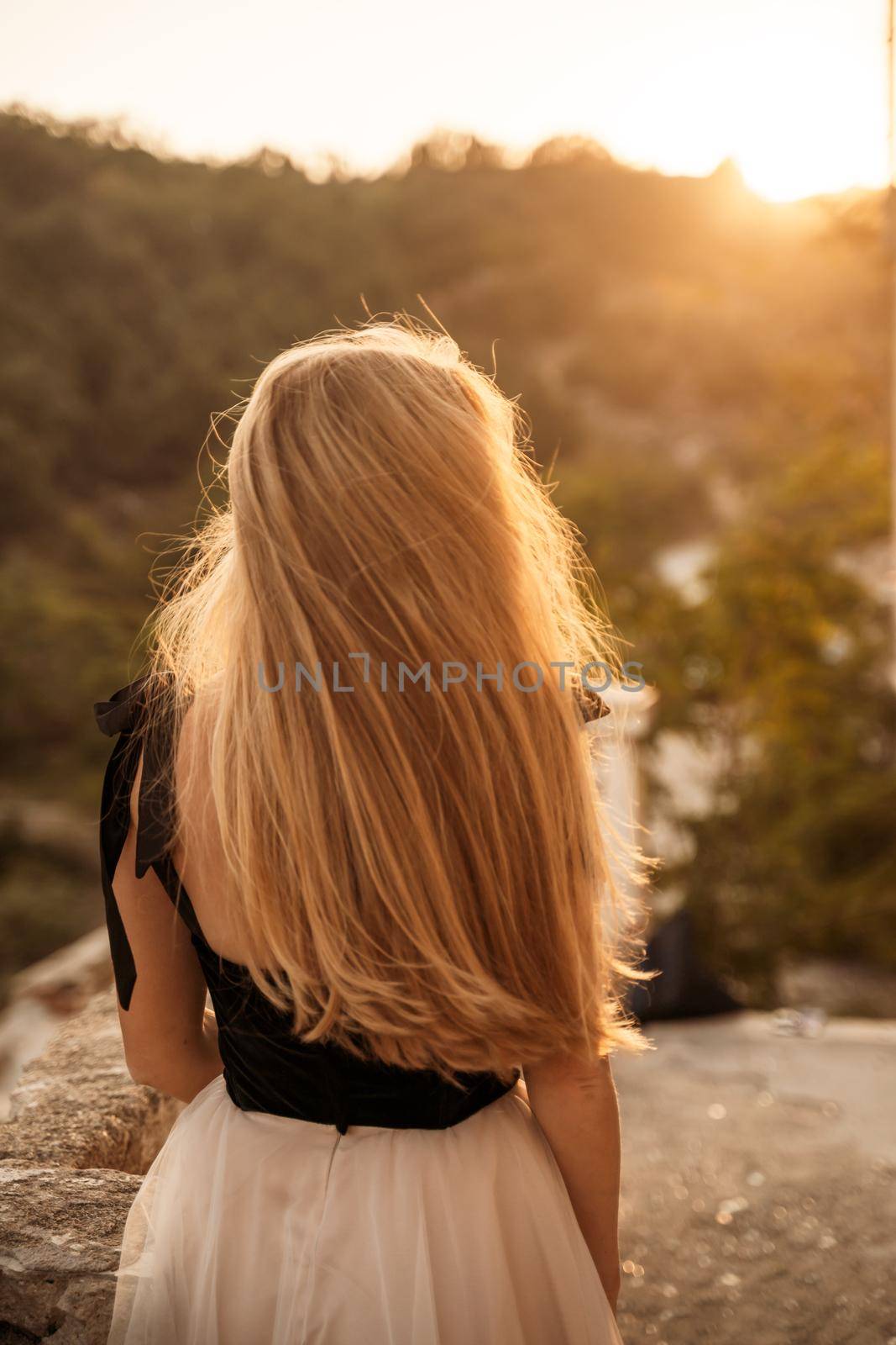 Blonde long hair, nature summer happy adult girl with long blond hair developing in the wind in nature. Dressed in a black top, white skirt. by Matiunina