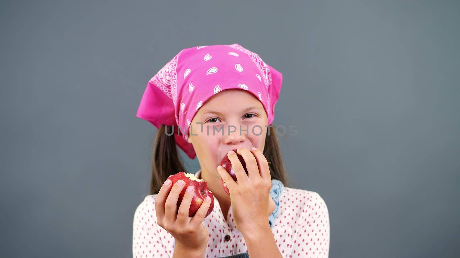 cute farmer girl holding in hands two large ripe red apples, eats, bites them on a gray background in the studio. Healthy nutrition concept. High quality photo