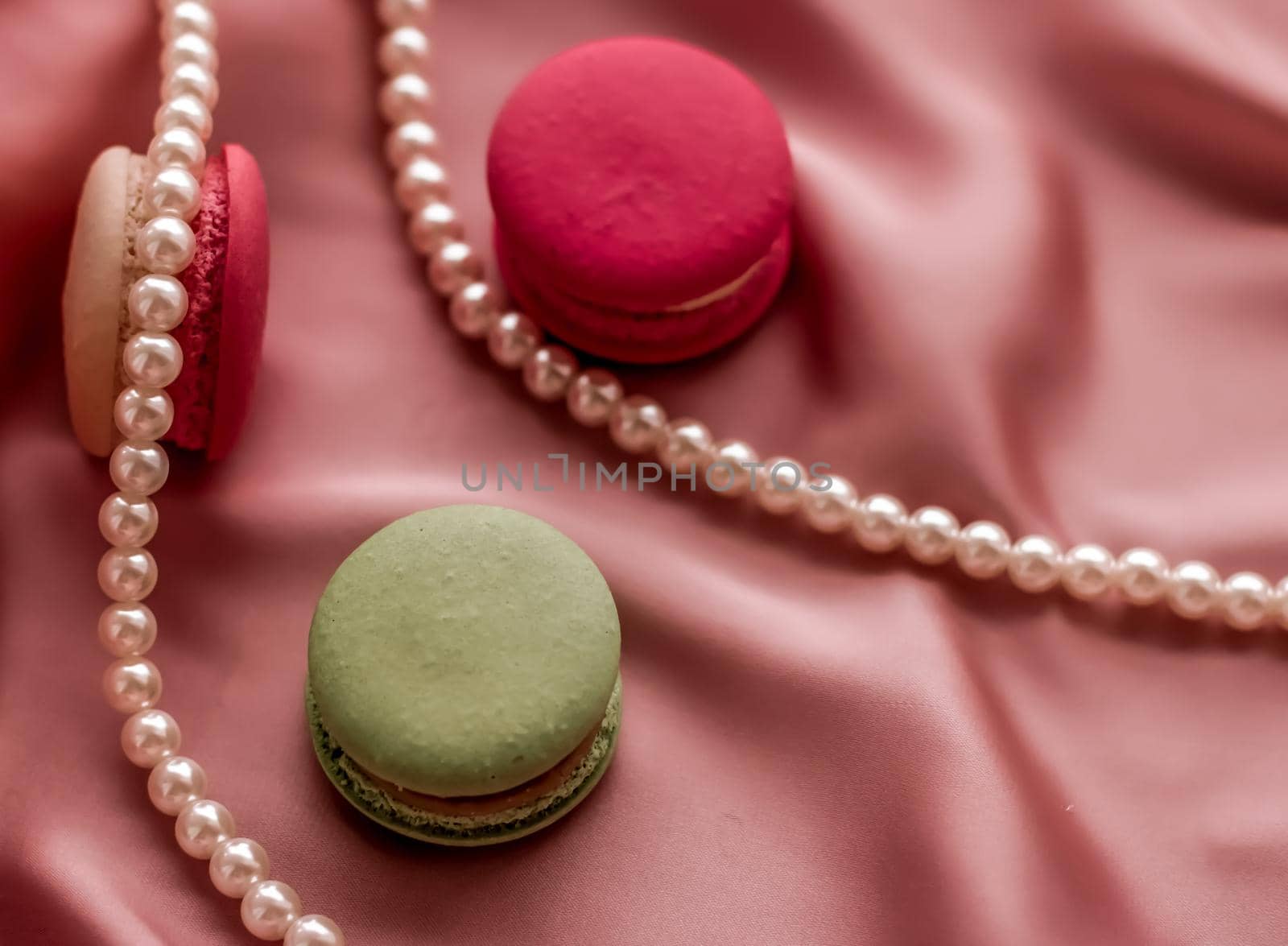 Girly, bakery and branding concept - Sweet macaroons and pearls jewellery on silk background, parisian chic jewelry, French dessert food and cake macaron for luxury confectionery brand, holiday gift