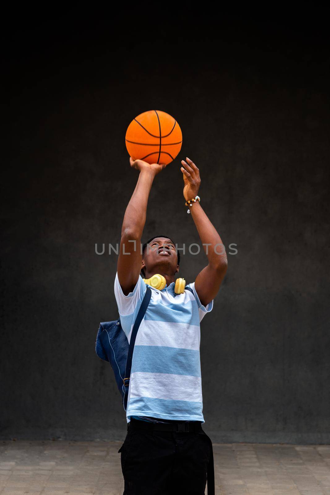 Vertical portrait of teen African American boy playing with a basketball ball outdoors. by Hoverstock