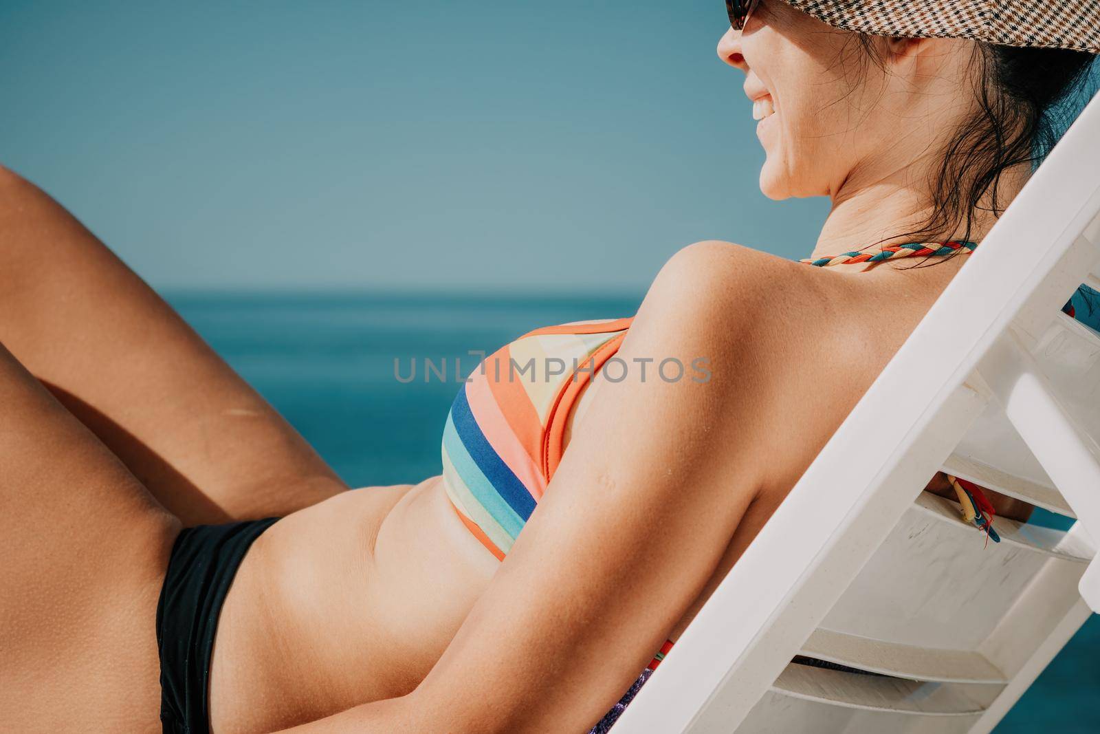 Woman in rainbow bikini. Happy tanned girl in rainbow swimsuit at seaside, blue sea water in background