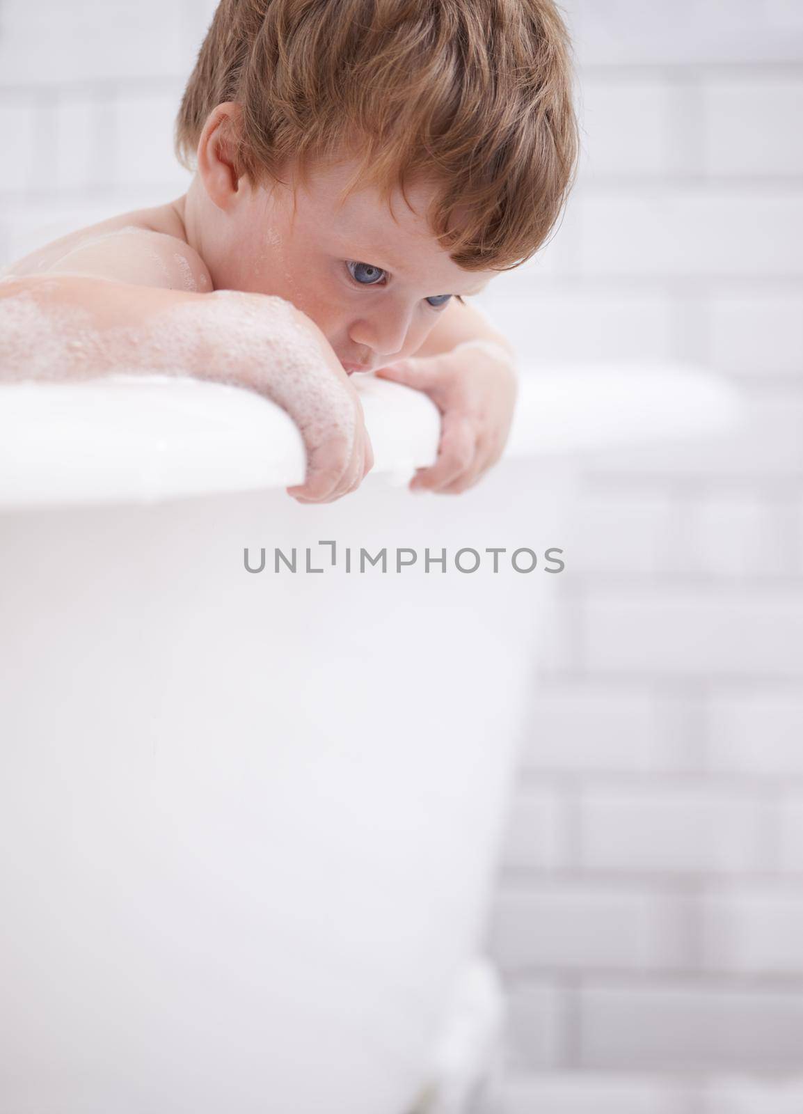 Getting fresh and clean. Tiny red-headed toddler in the bath tub. by YuriArcurs