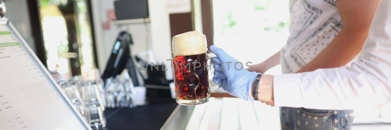 Close-up of waiter give glass with beer to client in protective glove, prevent covid spread. Bar, cafe or restaurant ground. Order, drink, beverage concept