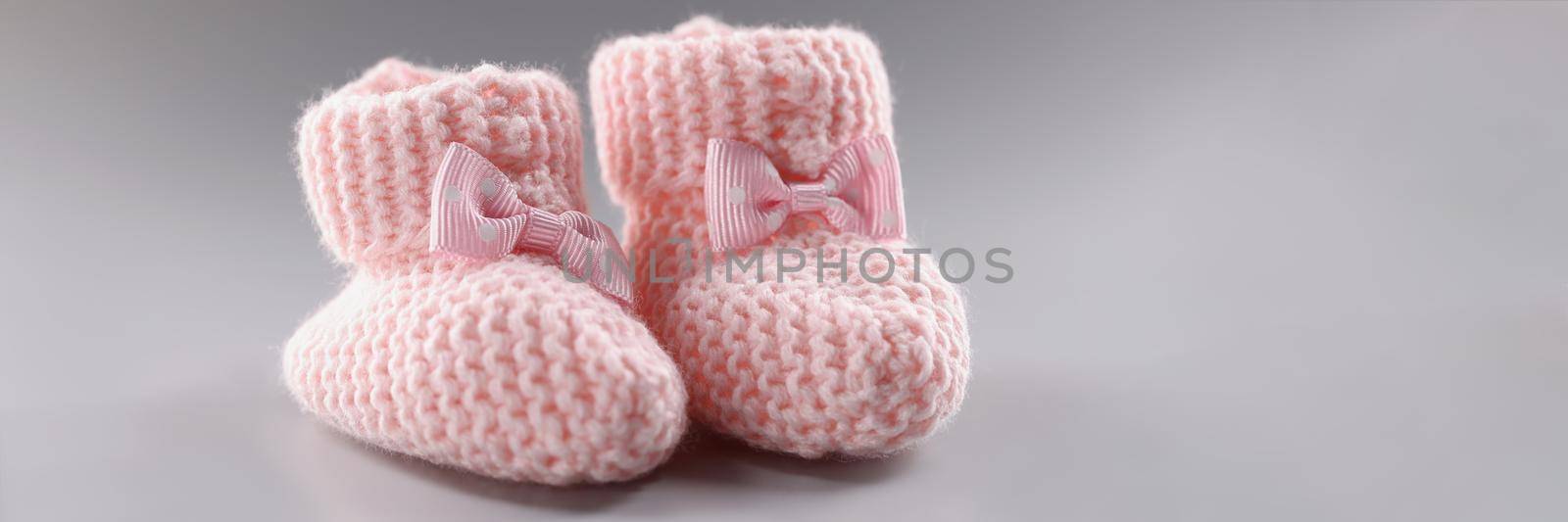 Close-up of pair of knitted pink baby booties with cute bow on it. Handicraft shoes for newborn baby on grey surface. Handmade, crochet, wool, care concept
