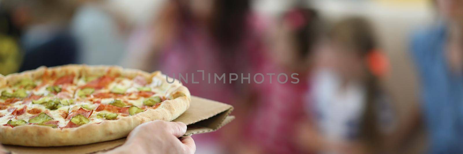 Close-up of man bring hot big pizza with stuffing and sauce. Smelly pizza with cucumber and cheese, order snack. Fast food, takeaway, hunger, party concept