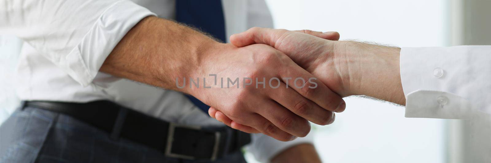Close-up of partners shake hands over business clipboard in office. Biz partners perform friendly gesture after successful agreement. Agreement concept