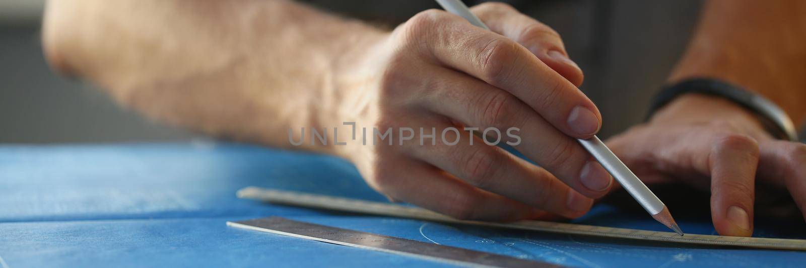 Close-up of builder man hand holding pencil and make corrections on building plan. Engineering blueprint design for buildings on desk. Architecture concept