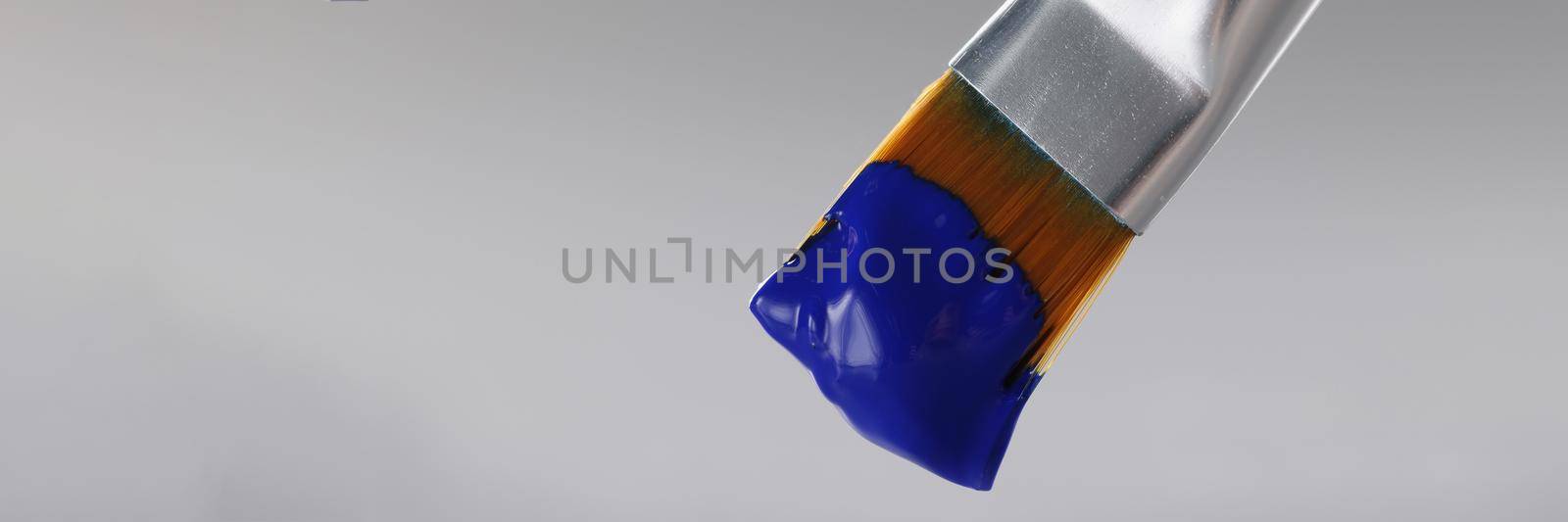 Close-up of brush with blue greasy oil paint on tip, professional equipment for drawing on grey background. Masterpiece, art, creativity, artistry concept