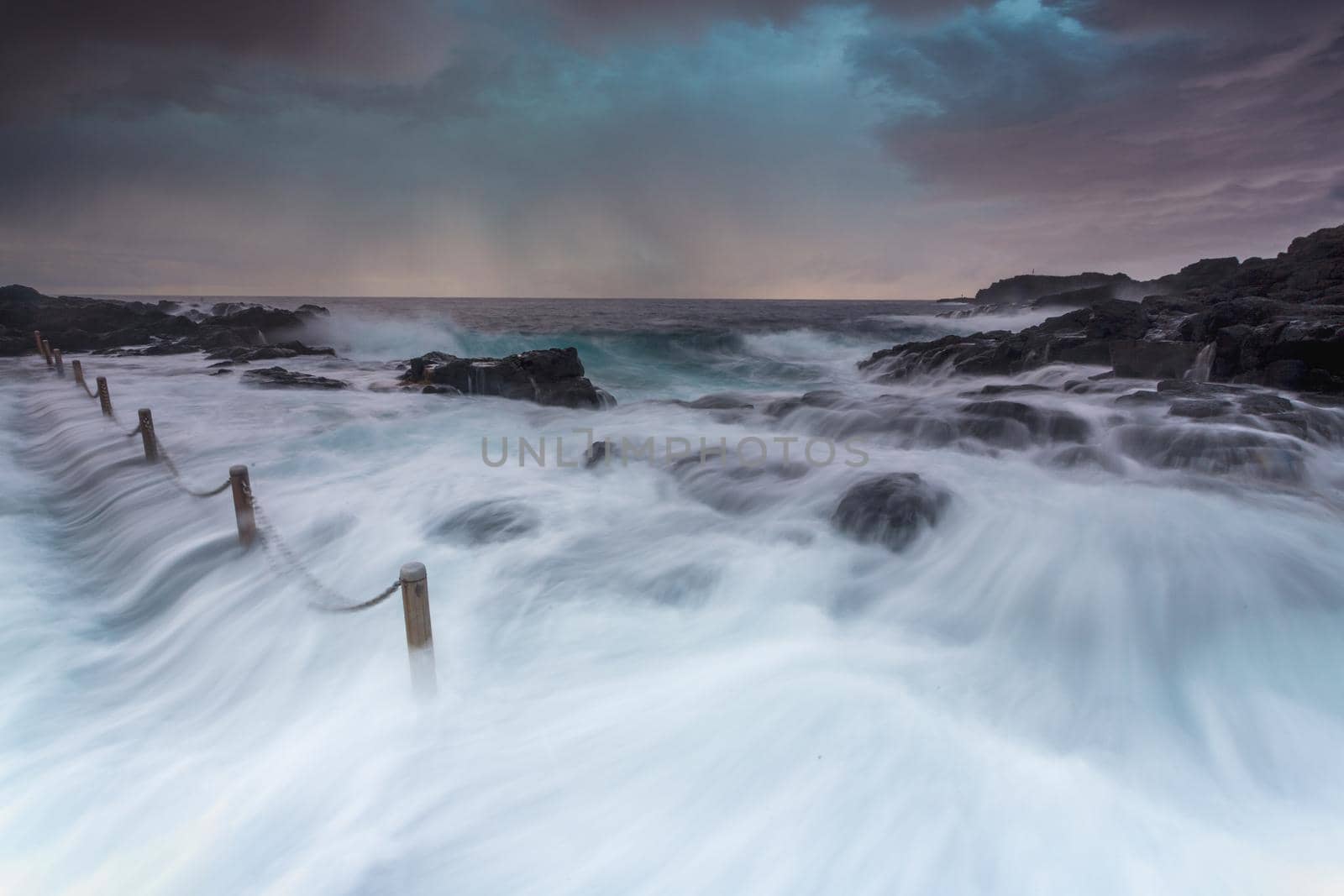 Large waves huge volume of water flowing over rocks and into rock pool, 
Long exposure with sunrise and rain clouds