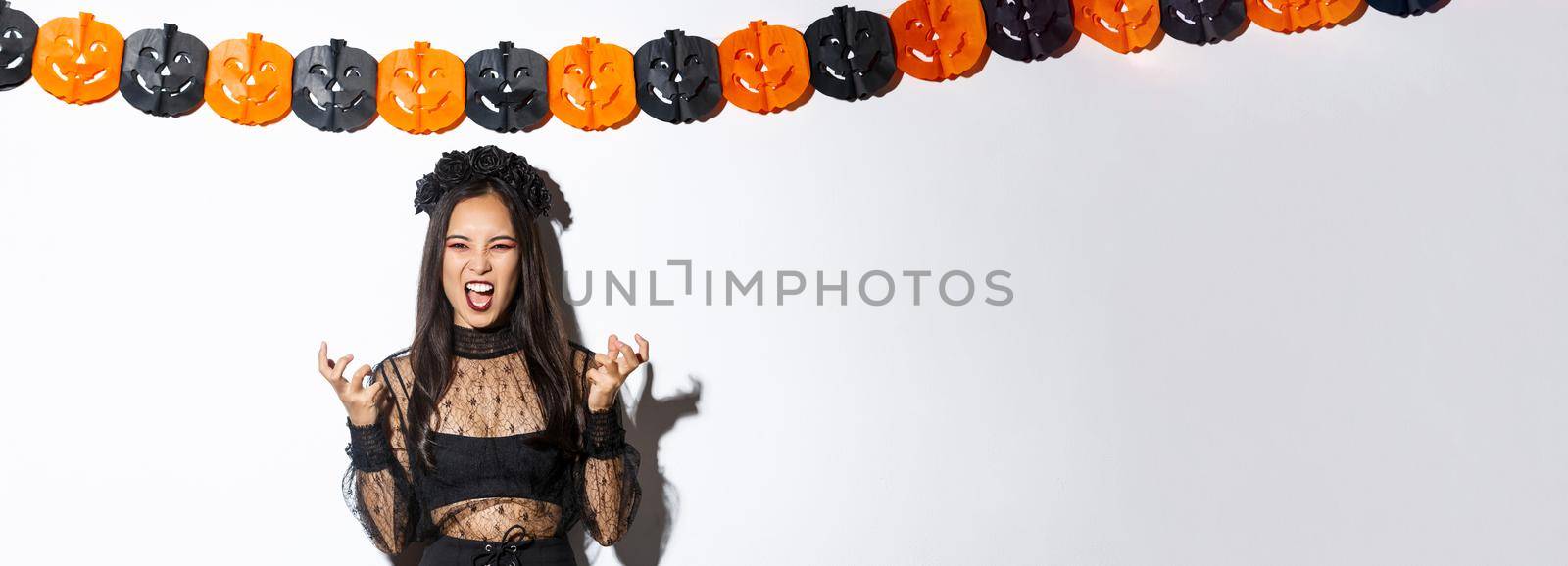 Image of wicked witch laughing evil and grimacing, woman celebrating halloween against party decorations, standing over pumpkin streamers.