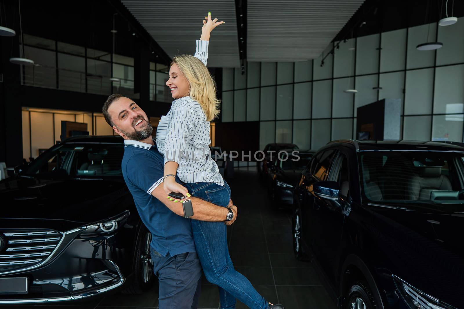 Happy caucasian couple hugging while buying a new car in a car dealership