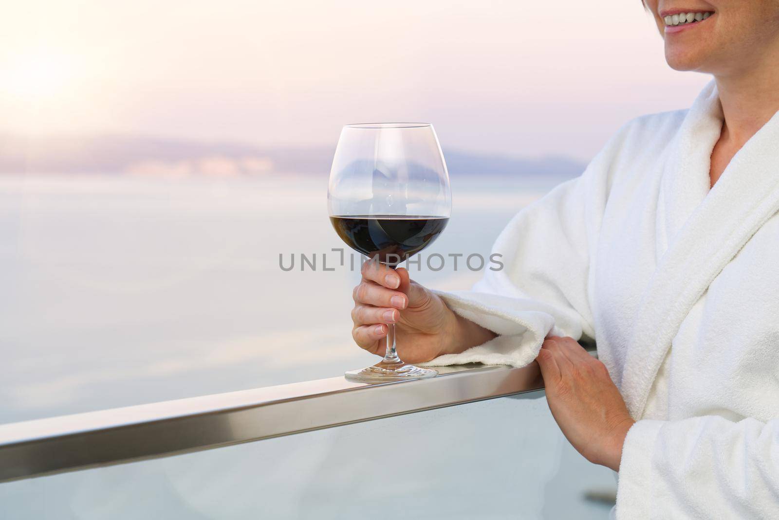 The elegant female hand holding a glass of red wine with the background of a sunny seaside view.