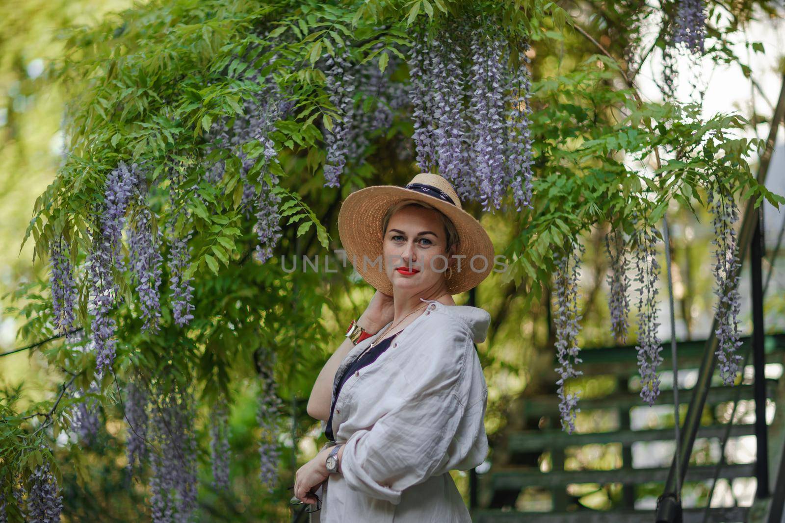 Thoughtful happy mature woman surrounded by chinese wisteria.