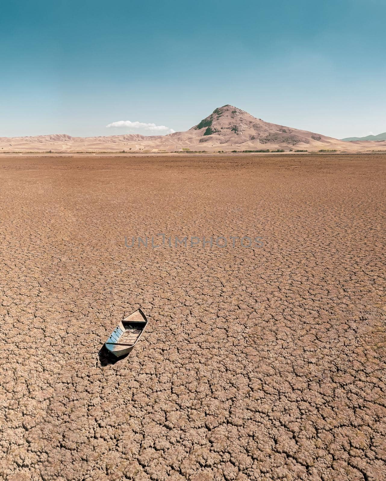 Abandoned row boat on cracked soil on lake bed dried up due to global warming and drought by Sonat