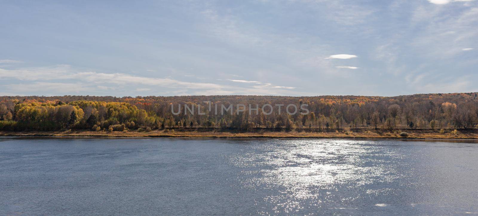 Beautiful, wide autumn river among forests and rocky shore. A calm and quiet place with autumn colors. Reflection of clouds in the water in good weather
