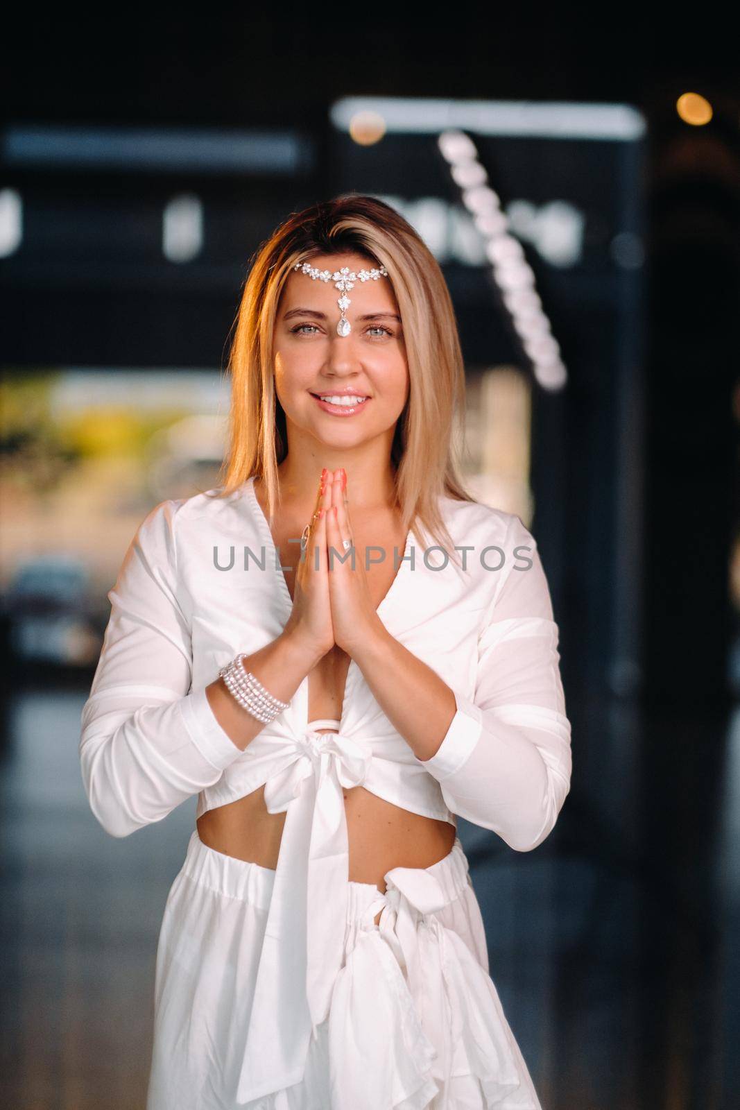 Portrait of a smiling girl in a white dress with her palms clasped in front of her.