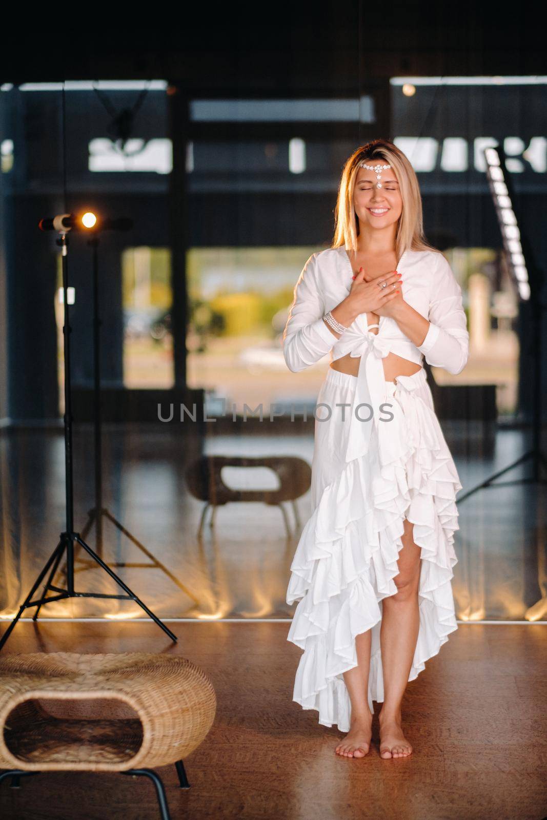 Portrait of a smiling girl in a white dress with her palms clasped in front of her.