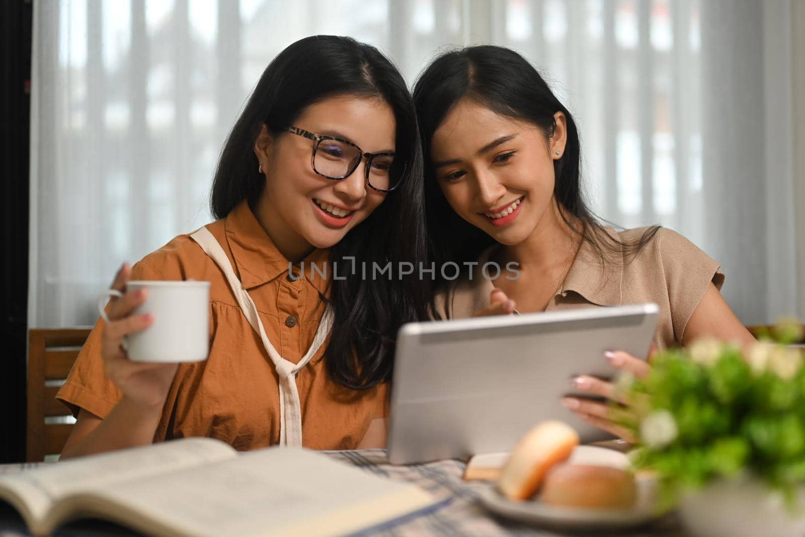 Two cheerful female students are searching online information on digital tablet for their research. Education and Technology concept.