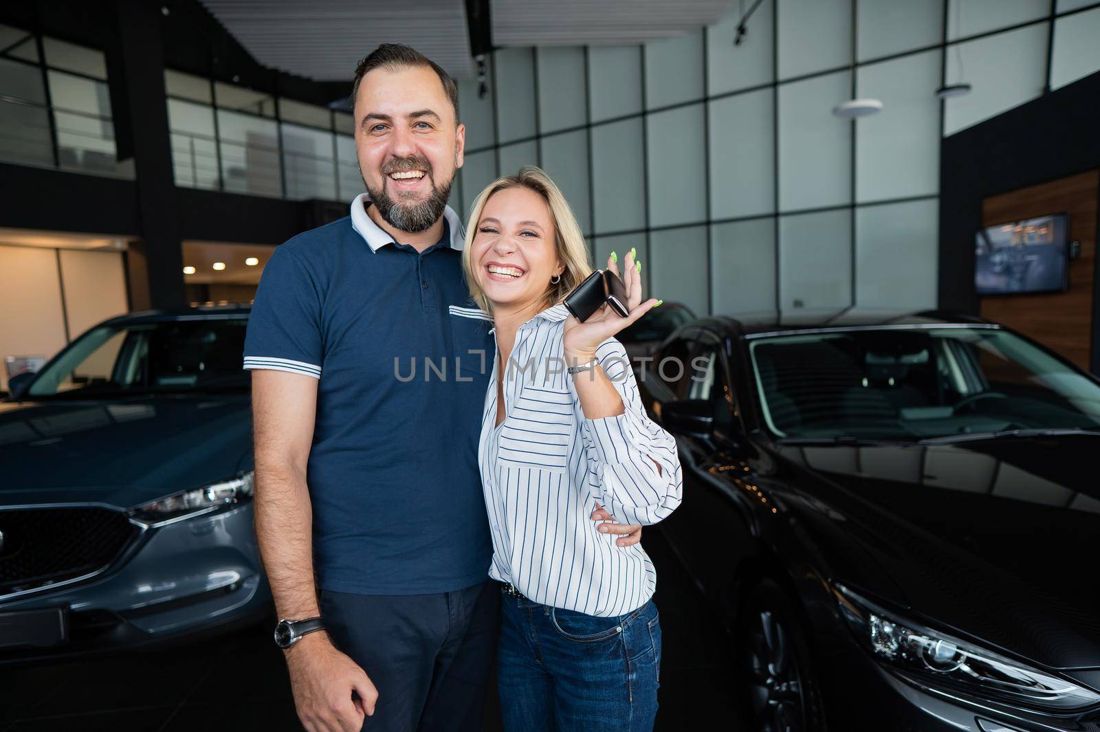 Happy caucasian couple hugging and woman holding new car keys in car showroom. by mrwed54