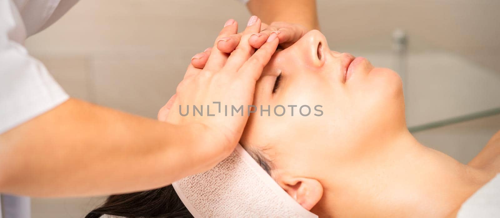 Facial massage. Young caucasian woman with closed eyes getting a massage on her forehead in a beauty salon. by okskukuruza