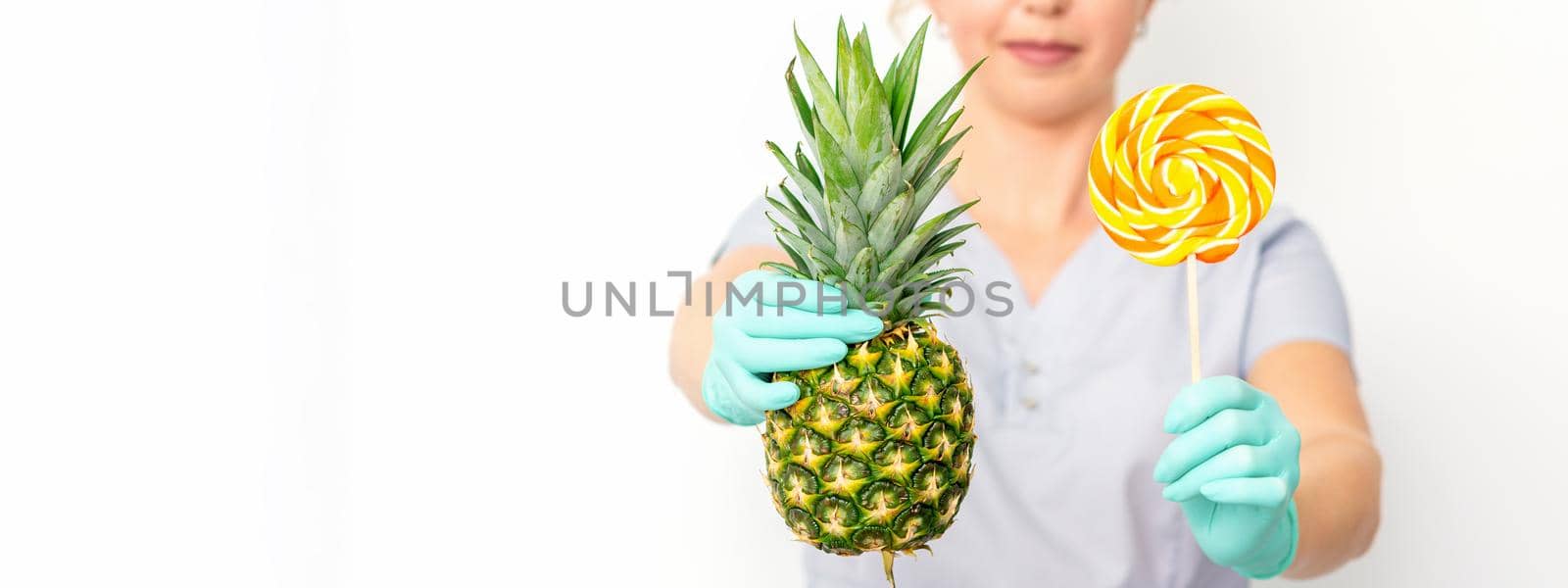 Young caucasian female doctor nutritionist holding fresh pineapple with lollipop over white background