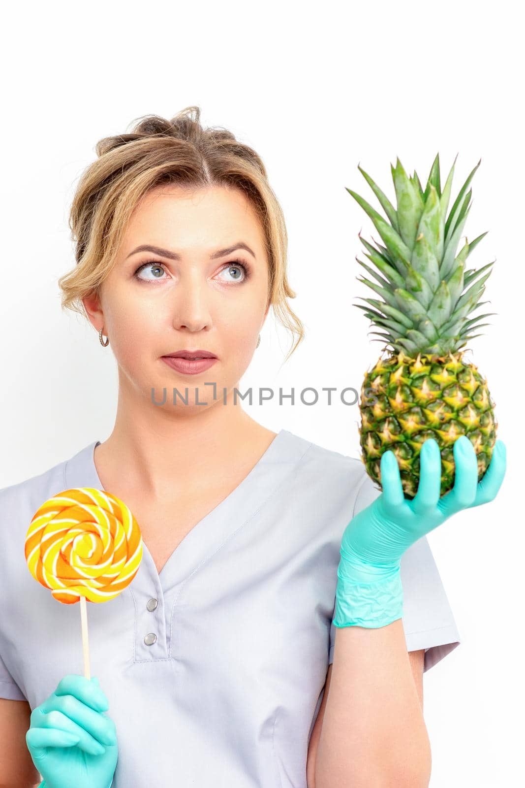 Young caucasian female doctor nutritionist holding fresh pineapple with lollipop over white background