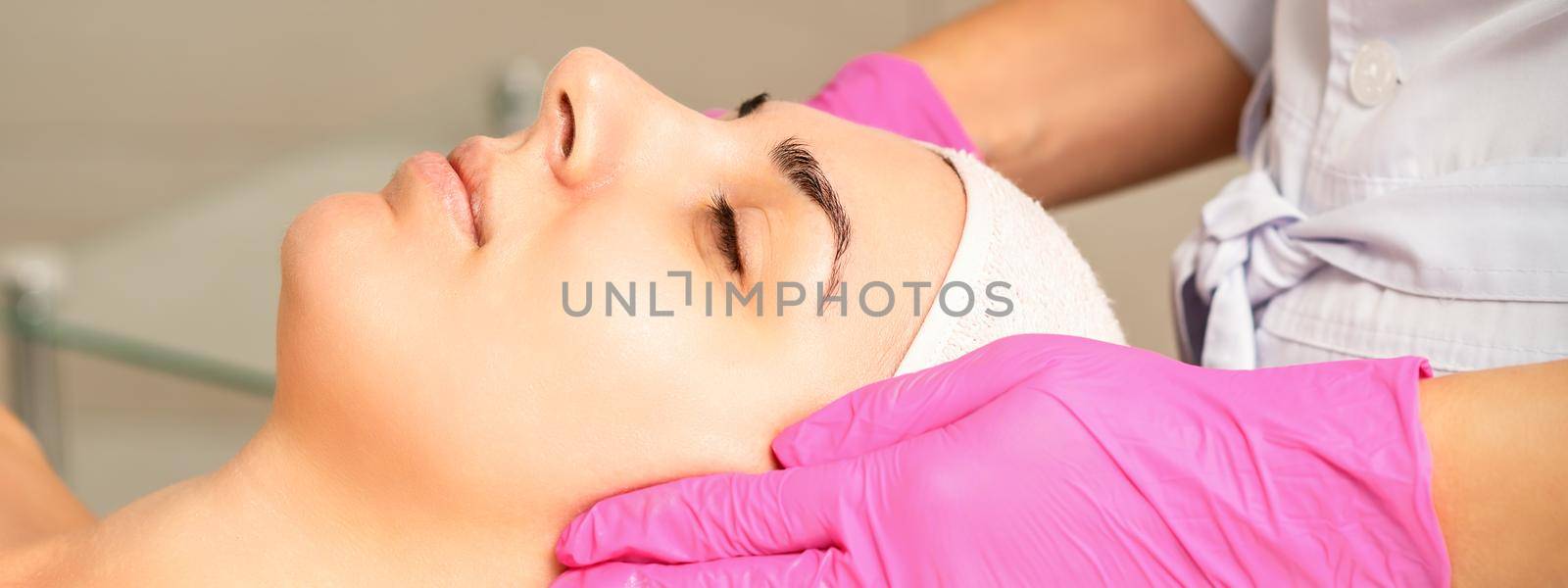 Cosmetologist with gloved hands applies a moisturizing mask with peeling cream on the female face. Facial cosmetology treatment. Procedures for facial care