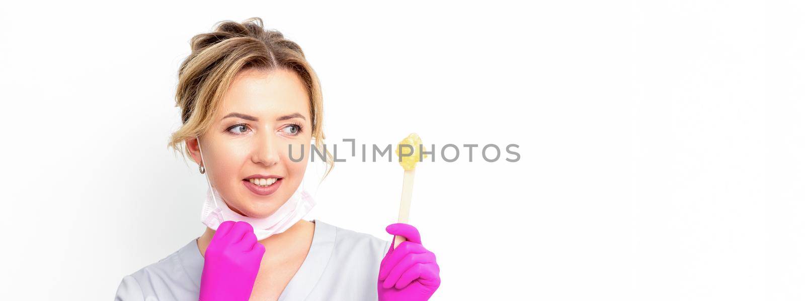 The master of sugar hair removal holds liquid yellow sugar paste, wax for depilation on a wooden stick on a white background