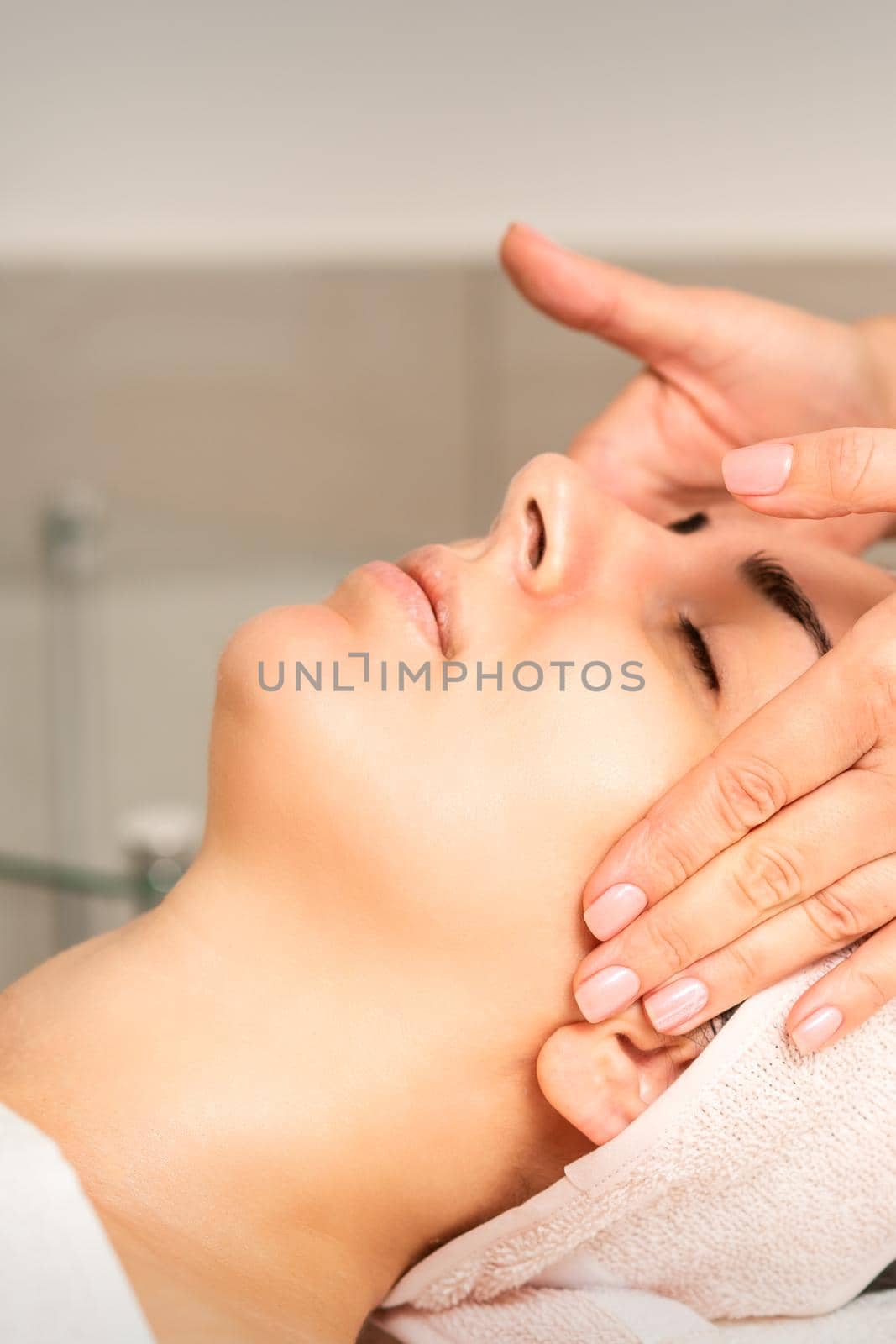 Young caucasian woman with closed eyes getting a facial massage in a beauty clinic. by okskukuruza