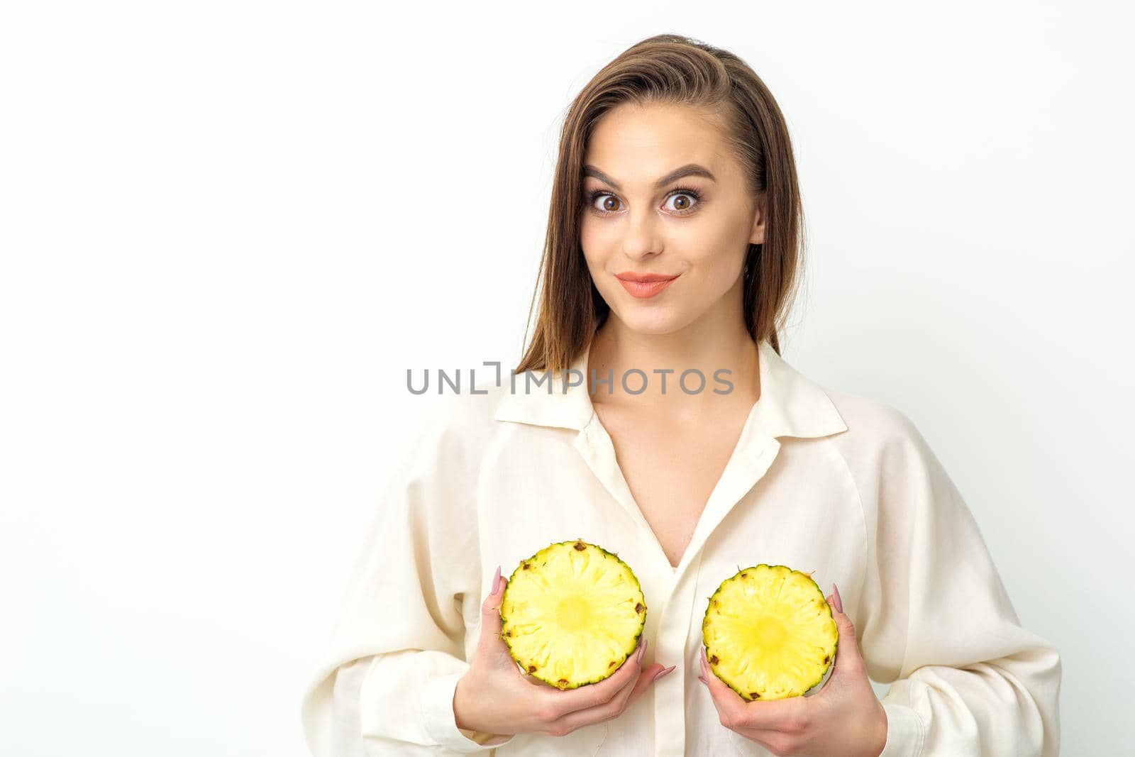 Young Caucasian smiling woman holding slices pineapple over white background, breast health concept