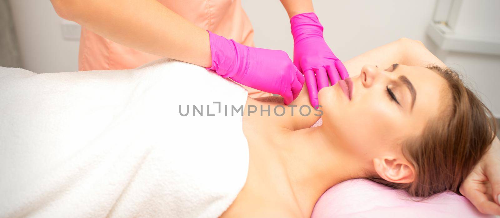 Waxing. Depilation under the armpits of the young woman lying with closed eyes in the spa salon. by okskukuruza