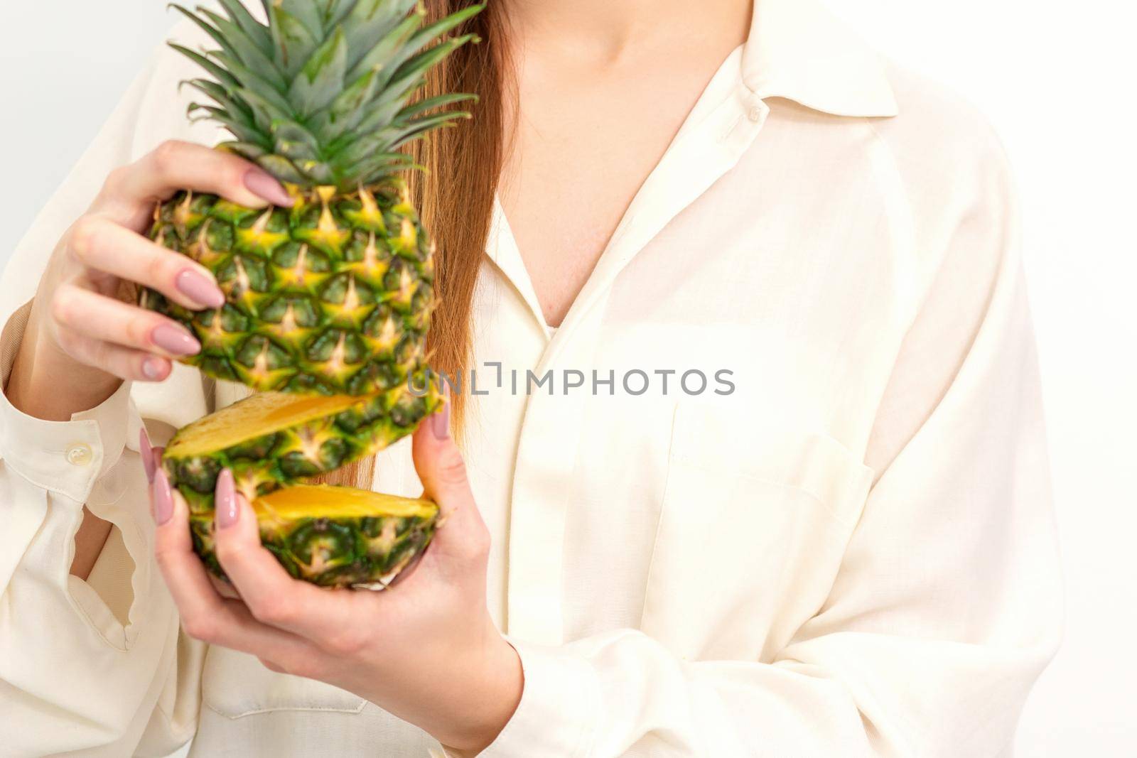 Beautiful young Caucasian woman holding pineapple and smiling, wearing a white shirt over white background