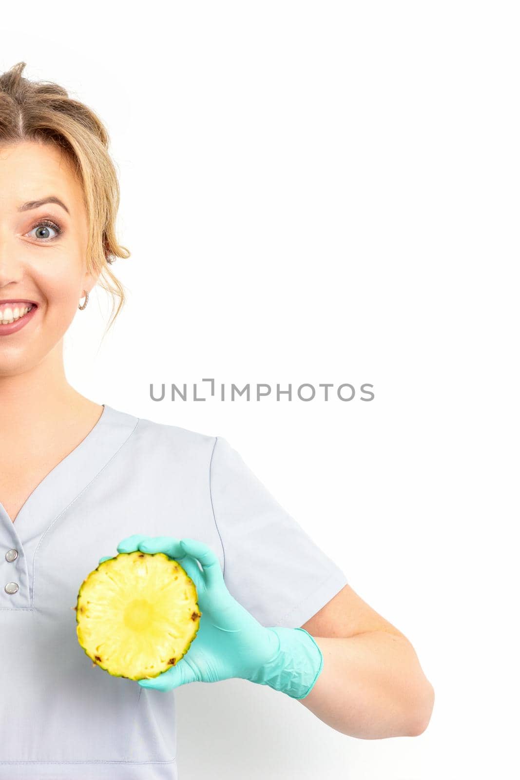 Young Caucasian smiling woman doctor nutritionist holding slices pineapple over isolated white background, breast health concept. by okskukuruza