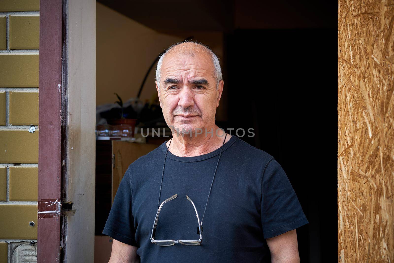 An elderly Caucasian craftsman with glasses on neck at the door of the workshop by jovani68