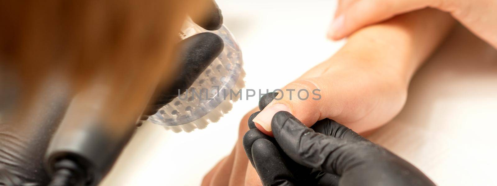 Hands of the manicure master removing dust from nails with a brush cleaning nails in a nail salon